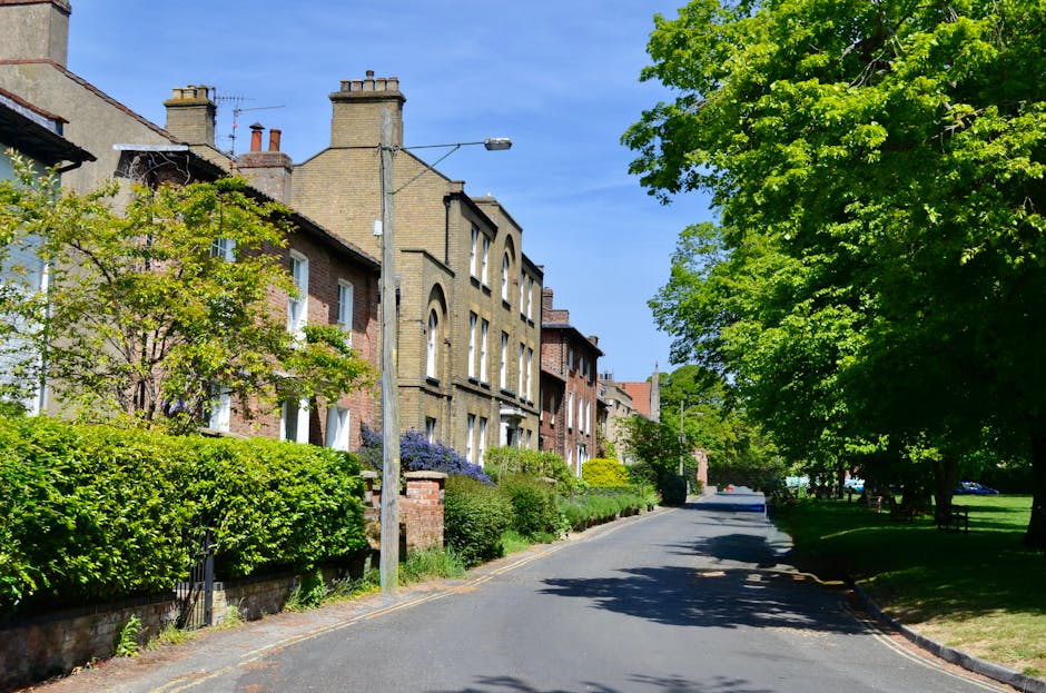 Aerial view of Feltham Hill Road in East Bedfont, showing a residential street with parked cars lined along the road and houses on both sides. The scene features a mix of terraced and semi-detached ho
